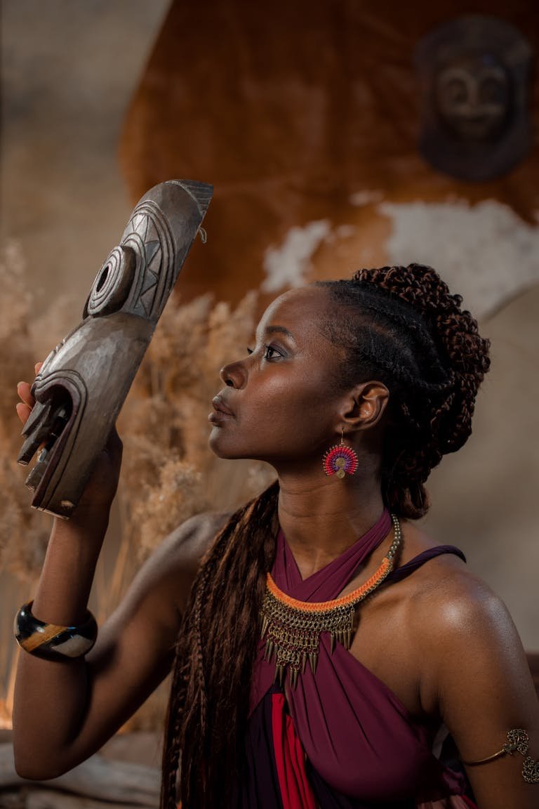 A beautiful African woman poses with a tribal mask, showcasing cultural elegance.