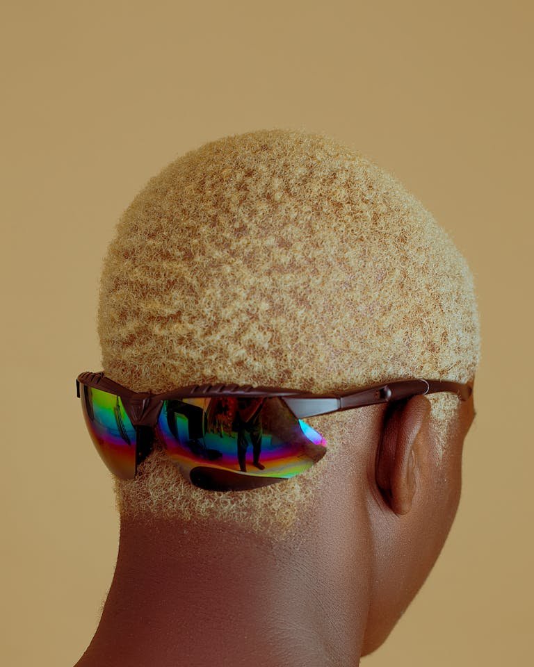 Close-up back view of a person with sunglasses against a yellow background, showcasing fashion style.