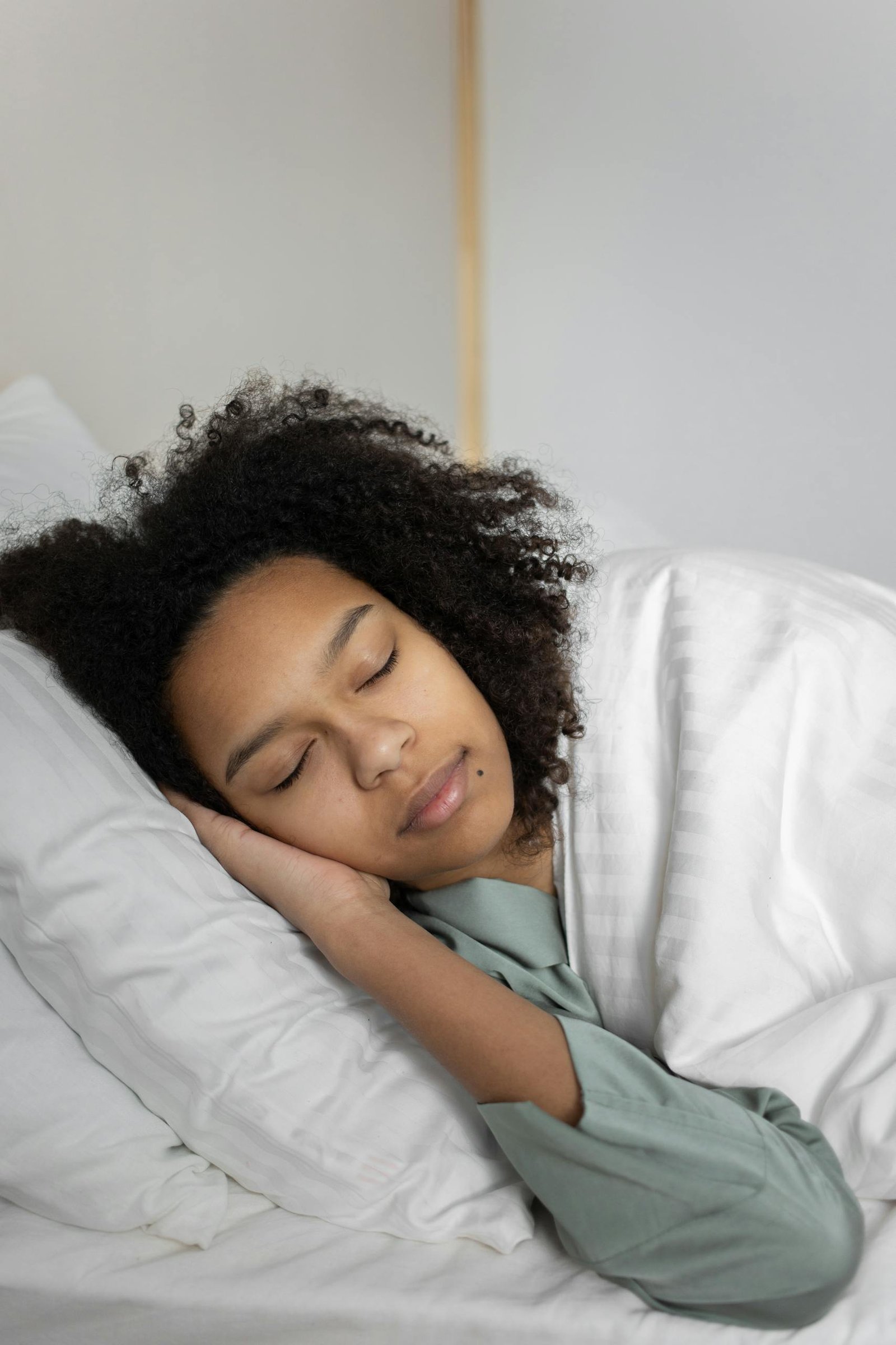 Relaxed woman with curly hair sleeping peacefully in a cozy bed.