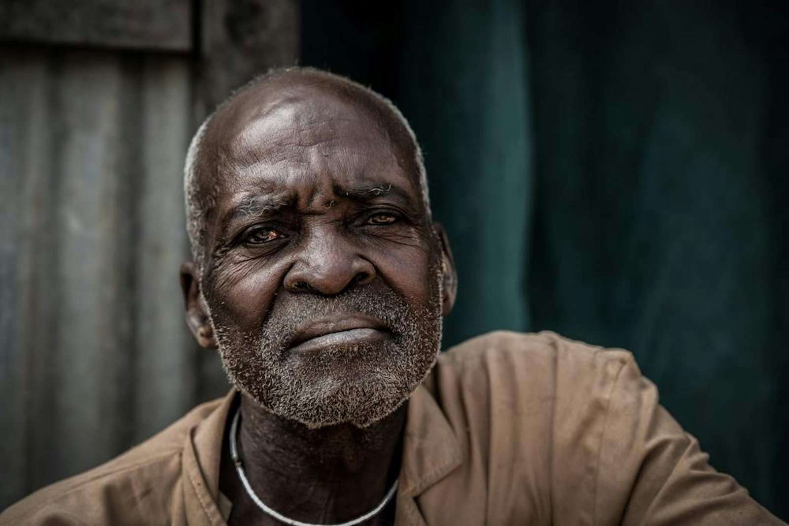A close-up portrait of an elderly man with a thoughtful expression against a rustic background.