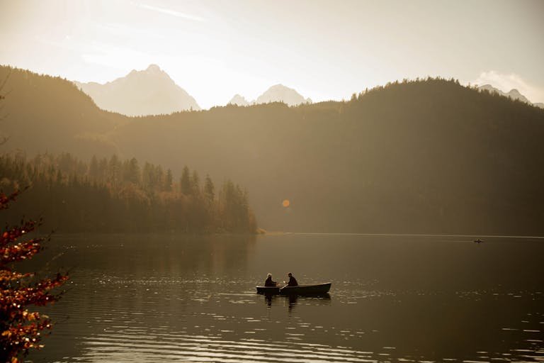 A couple enjoys a serene rowboat ride on a lake with a mountain backdrop near Schwangau, Germany.
