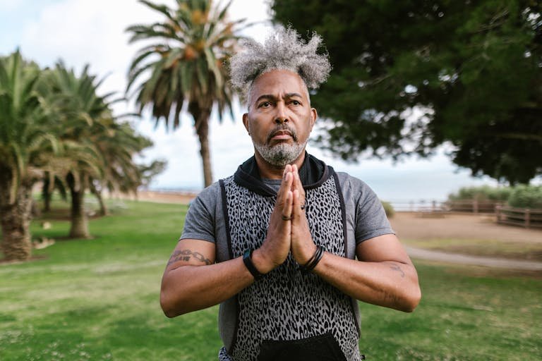 A senior man with afro hair meditates in a park, promoting wellness and health.