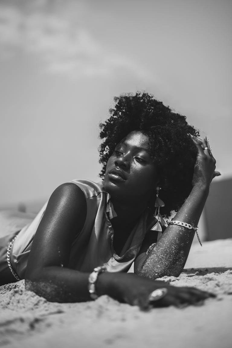 Elegant black and white portrait of a woman relaxing on the beach, exuding serenity and style.