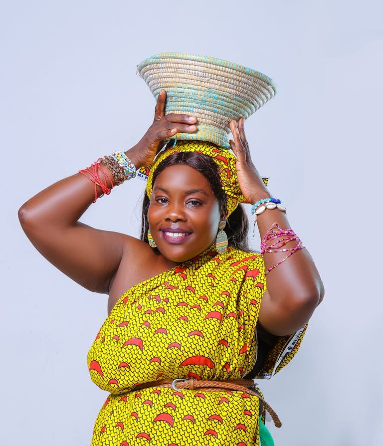 Joyful woman wearing vibrant African dress with a basket on her head, embracing cultural heritage.