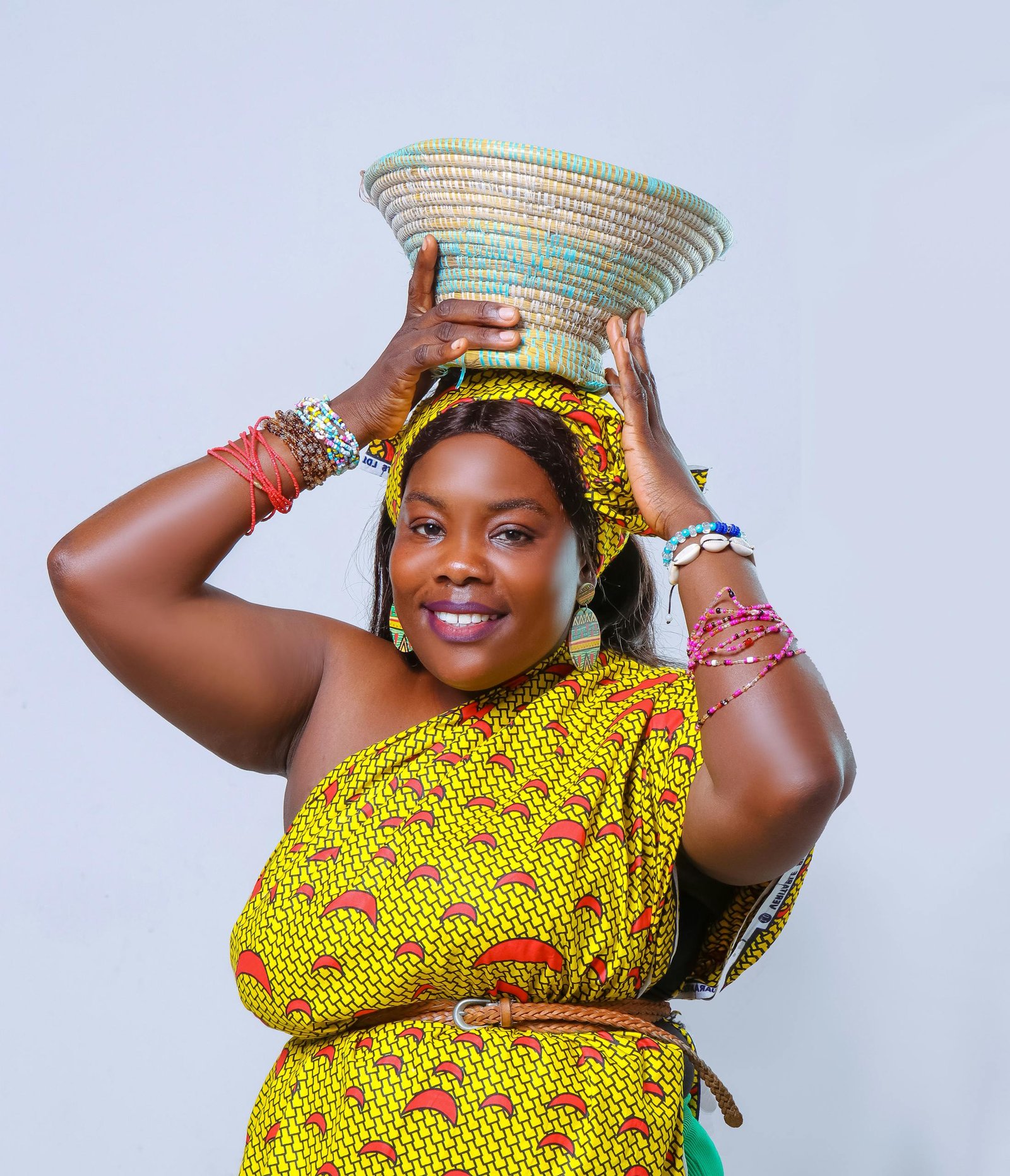 Joyful woman wearing vibrant African dress with a basket on her head, embracing cultural heritage.