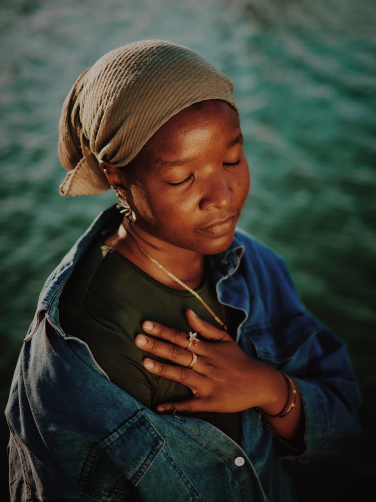 A serene portrait of a woman meditating by the river in Kaduna, Nigeria, displaying tranquility.