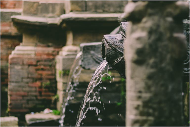 Intricately carved dhungedhara in Patan, Nepal with flowing water feature.
