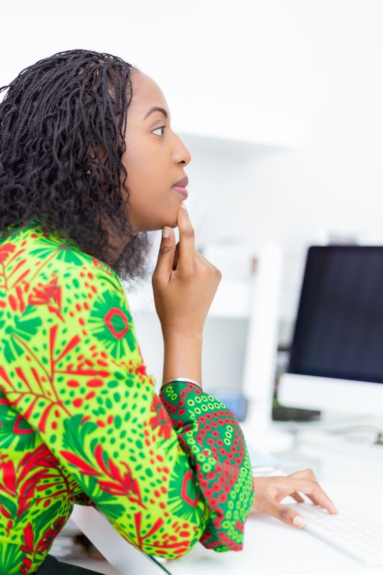 African woman in a bright green pattern dress, focused at her desk in an office setting.